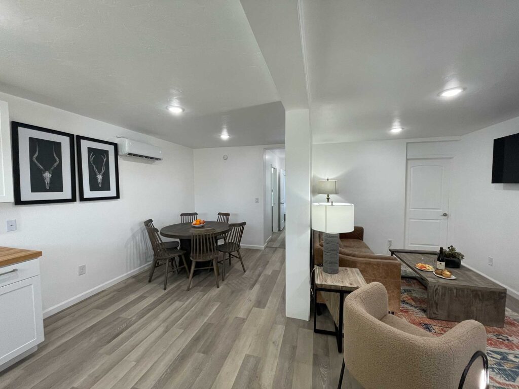 A bright, modern living space features a dining area with a wooden table, chairs, a couch, and decorative accents.